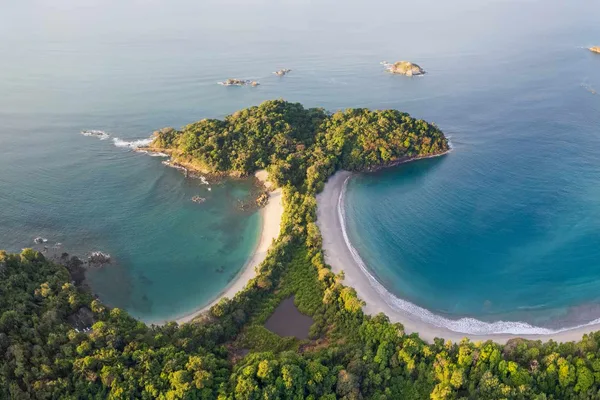 Aerial view of a forested headland in Manuel Antonio with twin sandy beaches and turquoise coves
