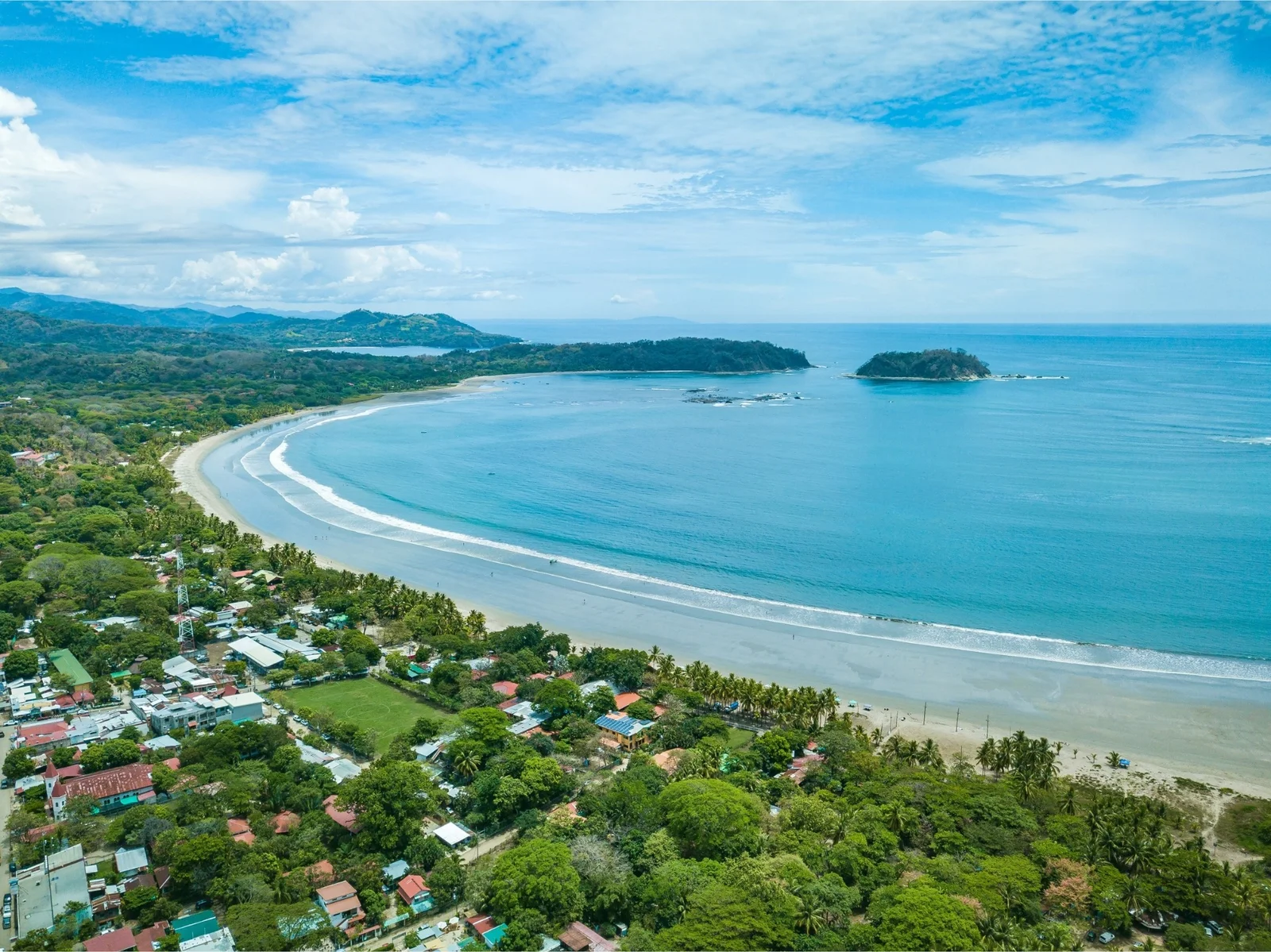 Aerial view of Samara's curved beach, turquoise bay, small island, and coastal town surrounded by trees