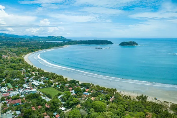 Aerial view of Samara's curved beach, turquoise bay, small island, and coastal town surrounded by trees