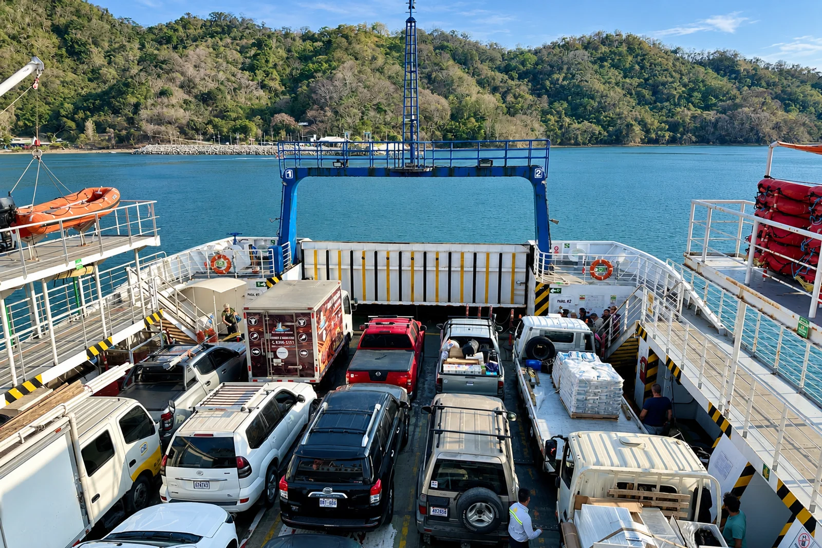 Cars and trucks loaded on a vehicle ferry deck, crossing a bay toward green hills