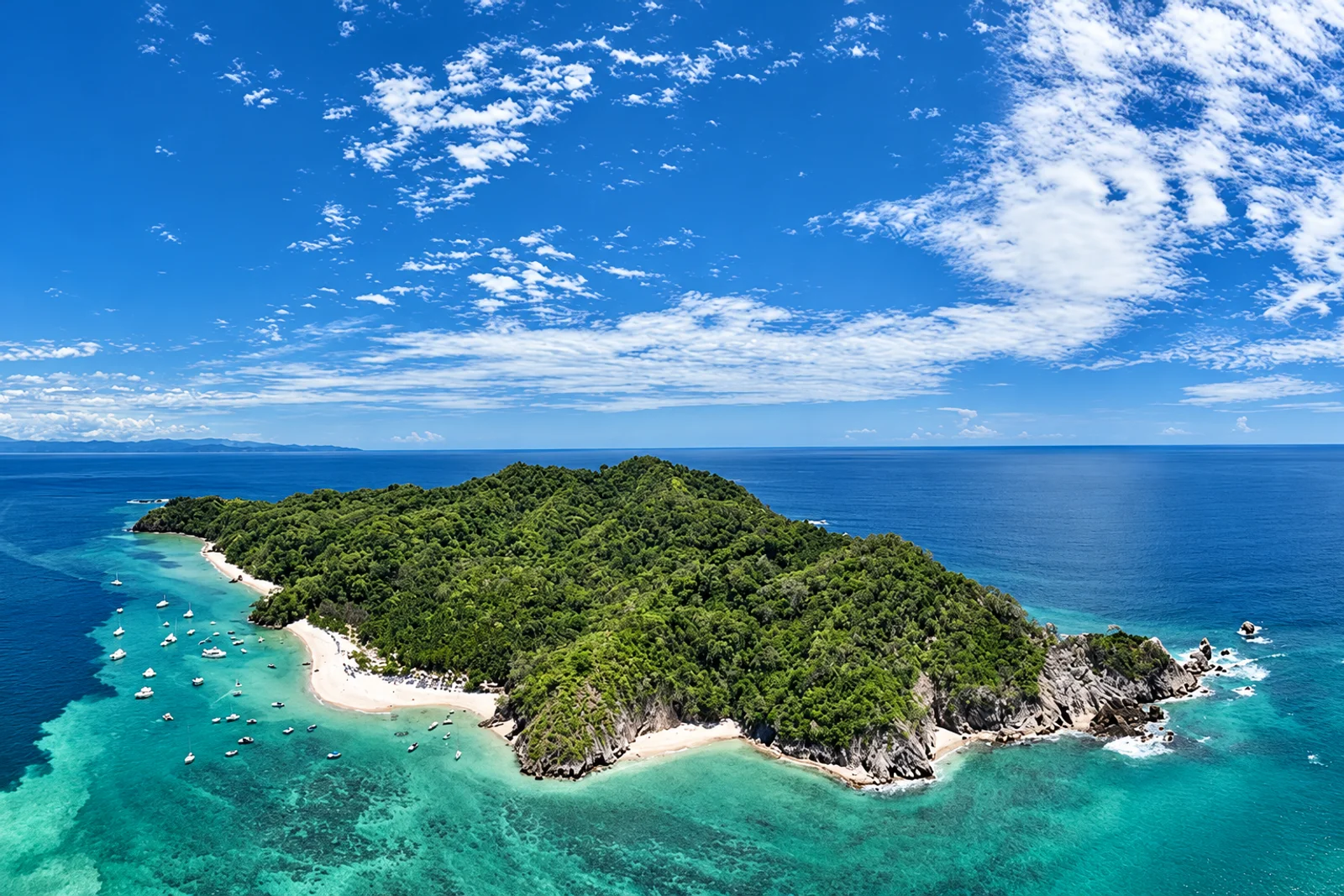 Aerial view of a forested island with white sand beaches and boats anchored in turquoise water