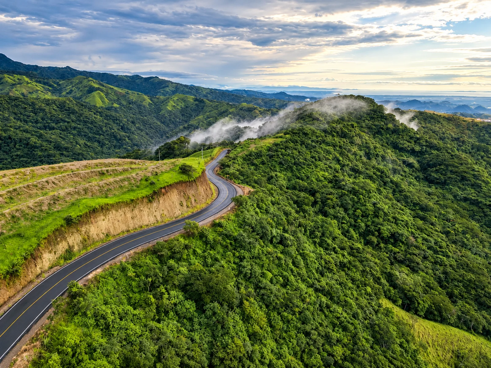 A winding mountain road curves along a ridge through lush green hills near Monteverde