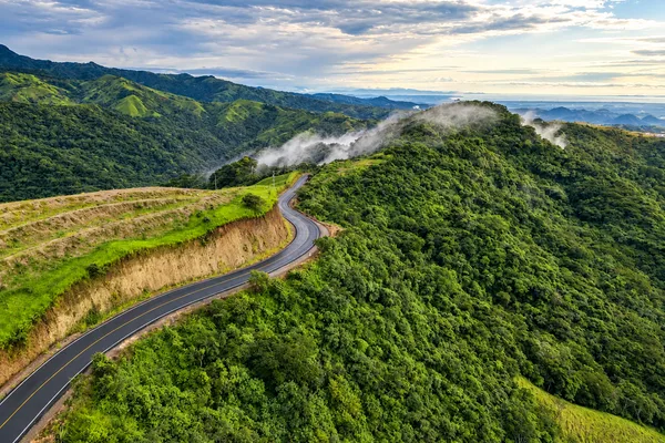 A winding mountain road curves along a ridge through lush green hills near Monteverde