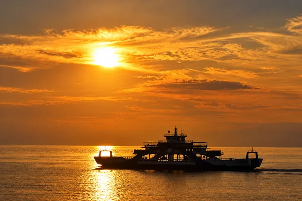 Silhouette of a car ferry crossing the water at sunset with a glowing orange sky