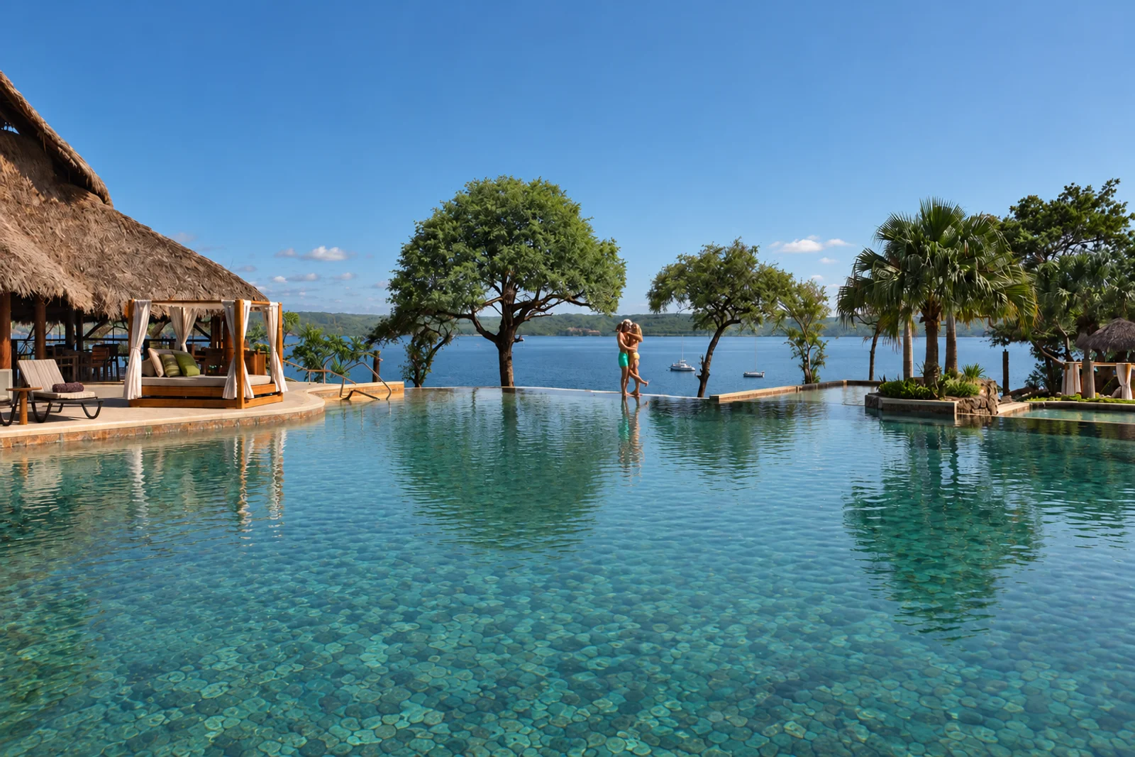 Couple embracing in an infinity pool overlooking the ocean, with a thatched-roof cabana and palm trees nearby